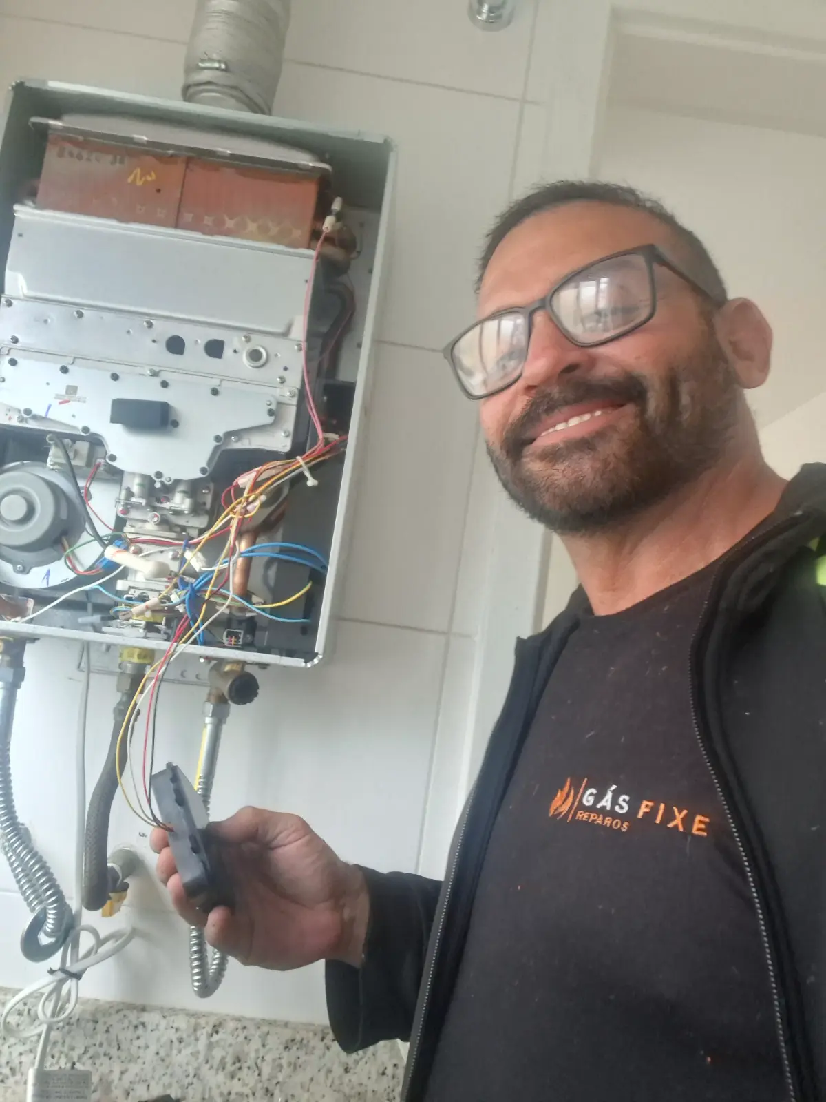 Técnico André Almeida sorrindo ao lado de aquecedor a gás aberto para manutenção